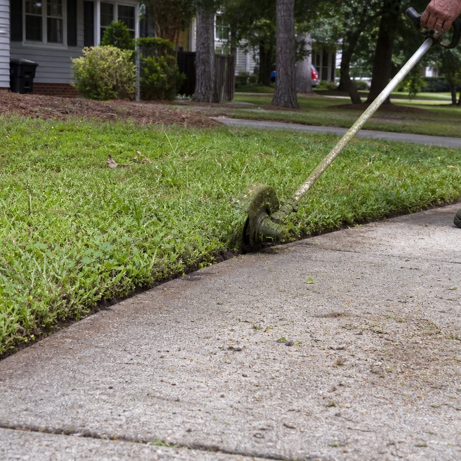 Trimming and edging along a concrete sidewalk for a clean lawn border